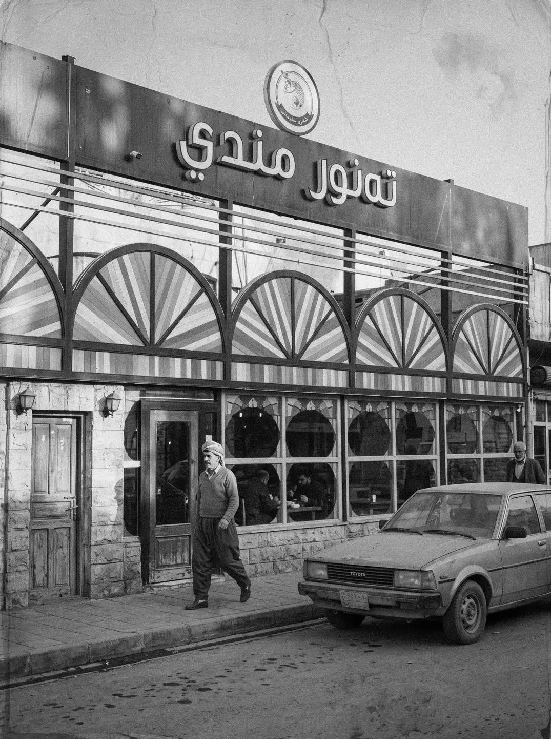 وێنەی ڕەش و سپی دەرەوەی چێشتخانەی تەنور مەندی